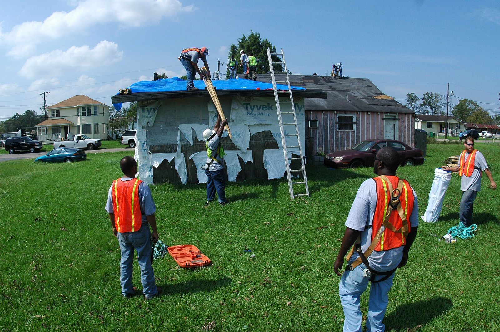 Crew in safety vests outside a storm-damaged house with its roof tarped