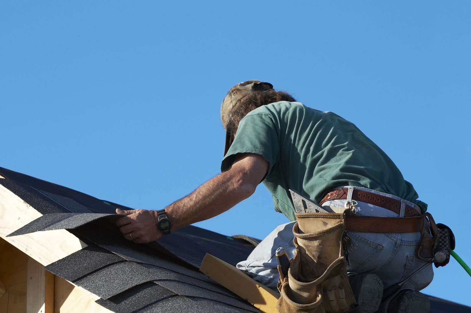 Roofer fastening architectural shingles on a pitched roof