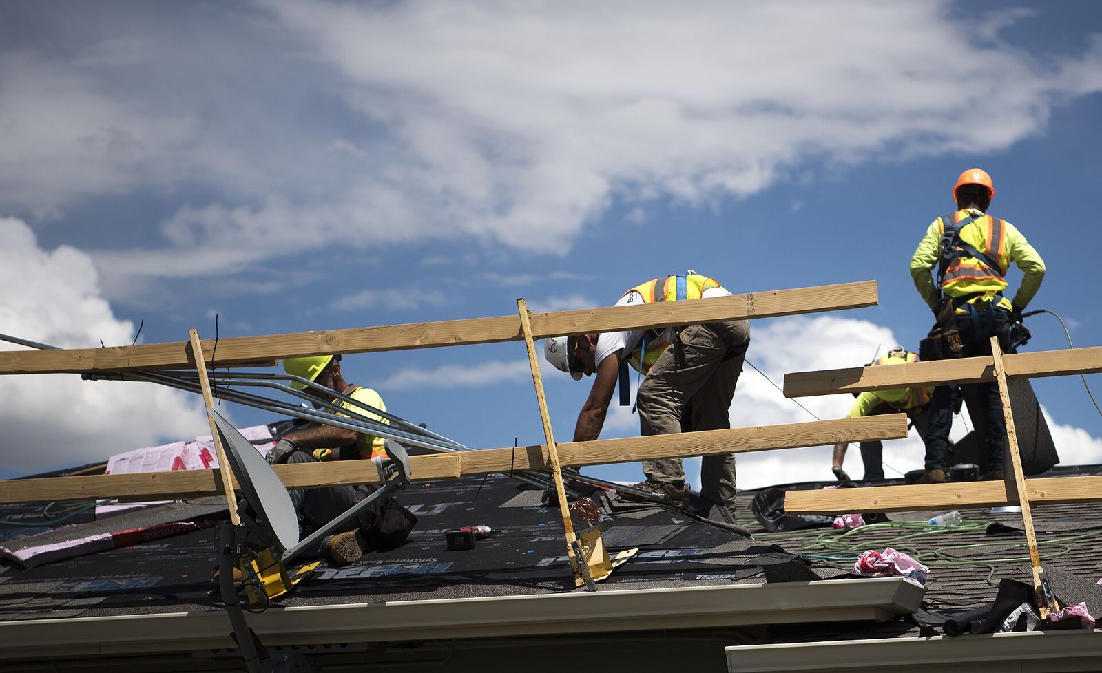 Crew setting new shingles on a roof under a cloudy sky